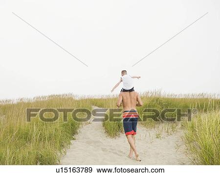 Stock Photo - Father carrying son on shoulders at beach. Fotosearch