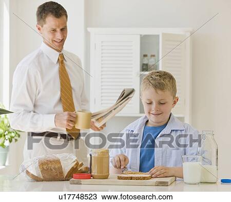 Stock Image - Father watching son make sandwich. Fotosearch