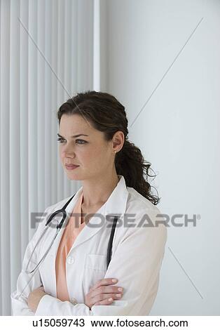 Stock Image - Female doctor looking out window pensively. Fotosearch