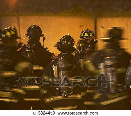 Stock Image - Firefighters standing outside burning building. Fotosearch