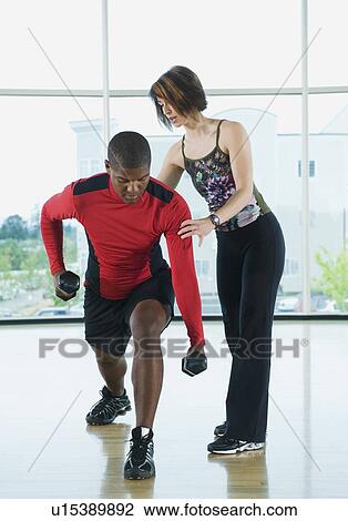 Stock Image - Fitness instructor helping man lunge with dumbbells. Fotosearch