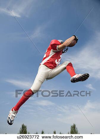 Football player in mid-air holding football View Large Photo Image Stock Image - Football player in mid-air holding football. Fotosearch