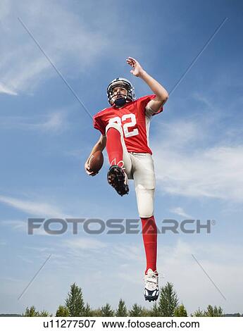 Football player in mid-air holding football View Large Photo Image Stock Photo - Football player in mid-air holding football. Fotosearch