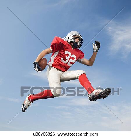 Stock Photograph - Football player in mid-air holding football. Fotosearch