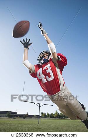 Football player in mid-air reaching for football View Large Photo Image Stock Photograph - Football player in mid-air reaching for football. Fotosearch