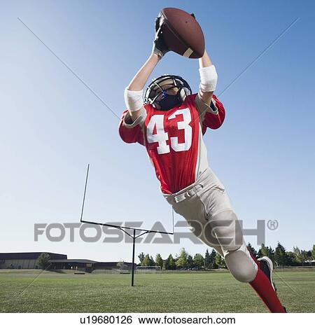 Stock Photograph - Football player in mid-air reaching for football. Fotosearch