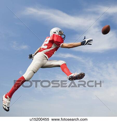Stock Photography - Football player in mid-air reaching for football. Fotosearch