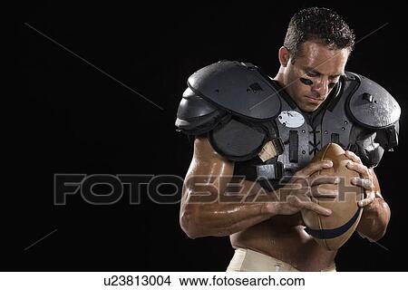 Picture - Football player wearing protective gear and holding football. Fotosearch