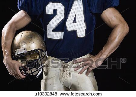Stock Photo - Football player wearing uniform and holding helmet. Fotosearch