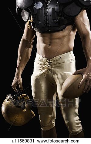 Stock Image - Football player with protective gear, football, and helmet. Fotosearch