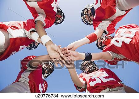 Picture - Football players joining hands in huddle. Fotosearch