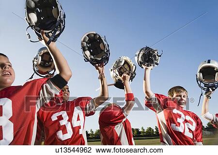 Stock Image - Football team holding helmets overhead. Fotosearch