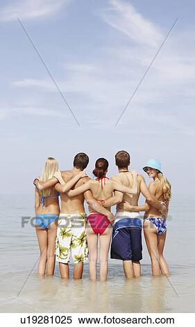 Stock Photography - Friends hugging and standing in ocean. Fotosearch