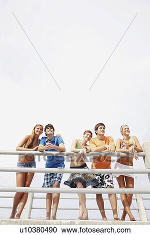 Stock Image - Friends leaning on boardwalk railing. Fotosearch