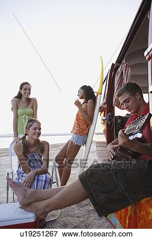 Stock Photo - Friends lounging around van on beach. Fotosearch