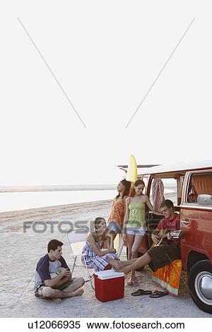 Stock Photography - Friends lounging around van on beach. Fotosearch