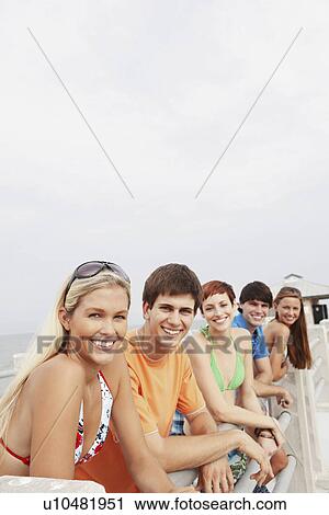 Stock Image - Friends posing on boardwalk railing. Fotosearch