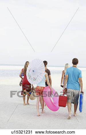 Stock Image - Friends walking with beach essentials. Fotosearch