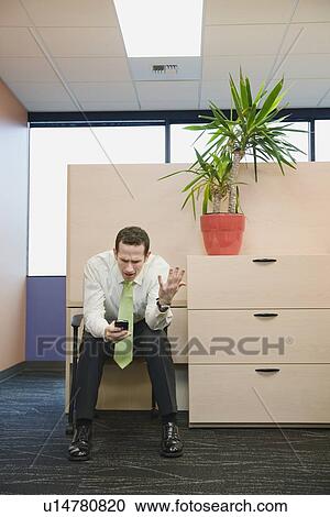 Stock Image - Frustrated businessman looking at cell phone. Fotosearch