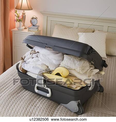 Stock Photograph - Full suitcase on bed. Fotosearch