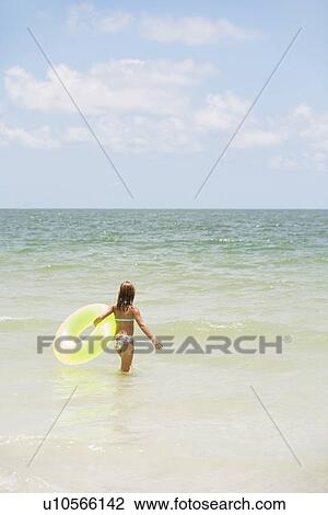 Girl carrying inflatable ring into ocean View Large Photo Image Stock Image - Girl carrying inflatable ring into ocean. Fotosearch