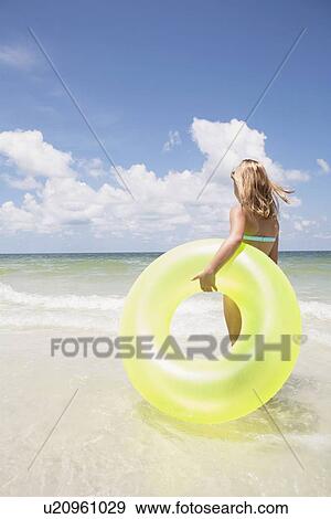 Stock Photo - Girl carrying inflatable ring into ocean. Fotosearch