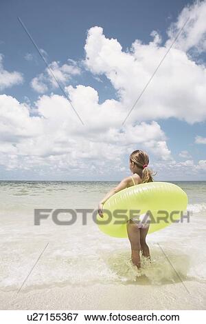 Stock Photo - Girl carrying inflatable ring into ocean. Fotosearch