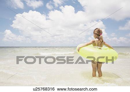 Girl carrying inflatable ring into ocean View Large Photo Image Stock Photograph - Girl carrying inflatable ring into ocean. Fotosearch