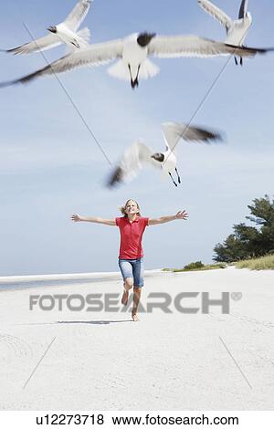 Stock Photo - Girl chasing birds on beach. Fotosearch