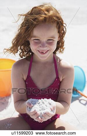 Stock Image - Girl digging in sand on beach. Fotosearch