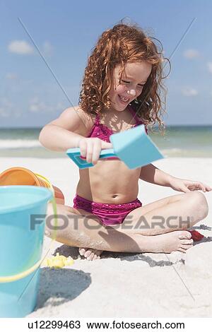 Stock Image - Girl digging in sand on beach. Fotosearch