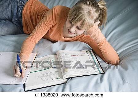 Stock Image - Girl doing homework on bed. Fotosearch