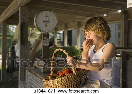 Stock Image - Girl eating fresh strawberries at farm stand. Fotosearch