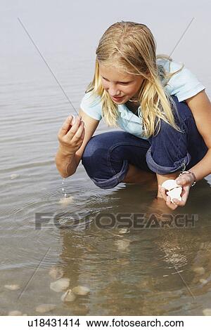 Picture - Girl finding seashells in ocean. Fotosearch