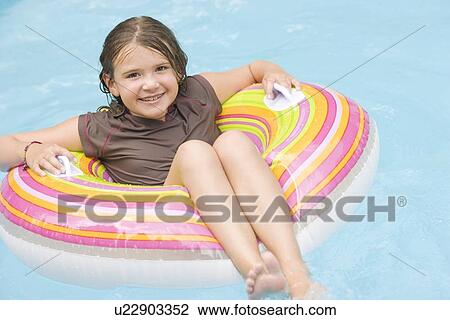 Stock Image - Girl floating in inflatable ring in swimming pool. Fotosearch