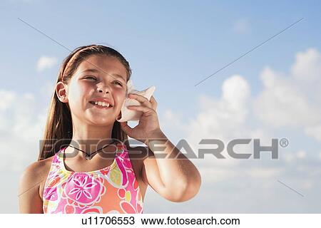 Stock Image - Girl holding conch shell to ear. Fotosearch