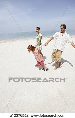 Girl holding hands with mother and father on beach View Large Photo Image Stock Image - Girl holding hands with mother and father on beach. Fotosearch