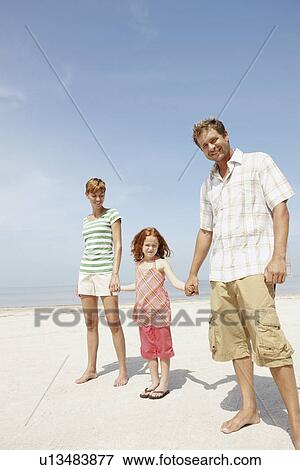 Stock Photo - Girl holding hands with mother and father on beach. Fotosearch