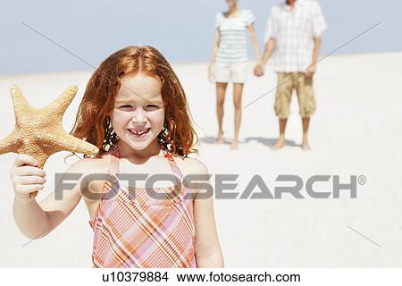 Picture - Girl holding up starfish on beach. Fotosearch