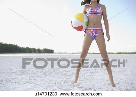 Stock Image - Girl in bikini jumping with beach ball. Fotosearch