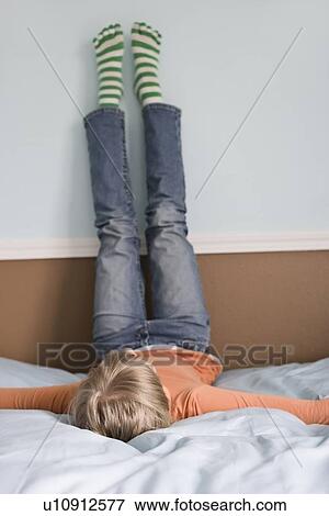 Stock Photo - Girl laying on bed with feet on wall. Fotosearch
