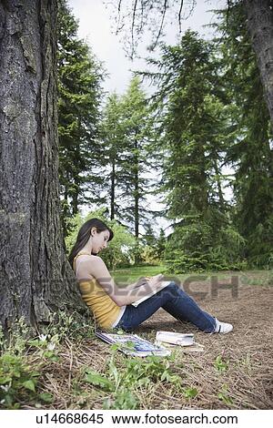 Stock Photography - Girl leaning against tree writing in notebook. Fotosearch