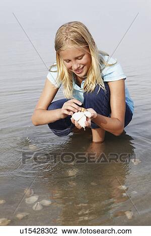 Stock Image - Girl looking for shells in shallow water. Fotosearch