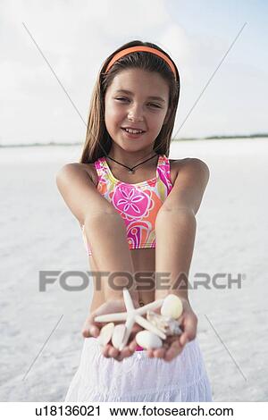 Stock Image - Girl on beach holding delicate starfish and shells. Fotosearch
