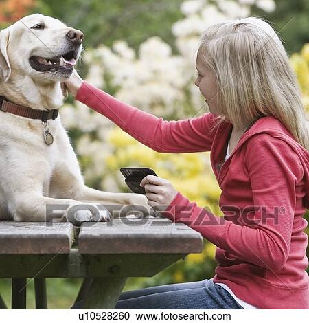 Stock Image - Girl petting dog sitting on picnic table. Fotosearch
