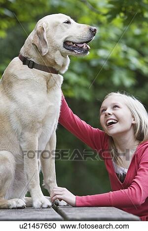 Stock Image - Girl petting dog sitting on picnic table. Fotosearch