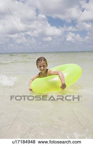 Stock Photo - Girl playing in inflatable ring into ocean. Fotosearch