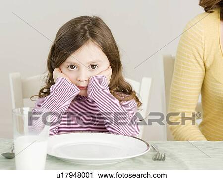 Stock Image - Girl sitting at dinner table. Fotosearch