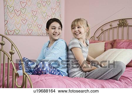 Picture - Girl sitting back to back on bed. Fotosearch