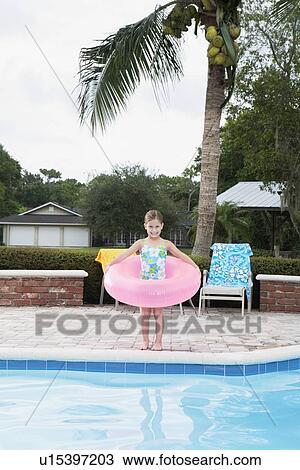 Stock Image - Girl standing at edge of swimming pool with inflatable ring. Fotosearch